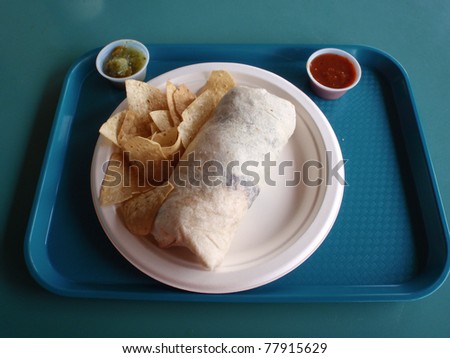 Burrito and Chips on Paper plate with small cups of red and green sauce on blue tray on a blueish-green table.