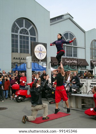 SAN FRANCISCO- JANUARY 16: performers put on a show as a man balances his sister on his shoulders tries to pass her to a man squatting from crowd January 16, 2010 at Ferry Building San Francisco.