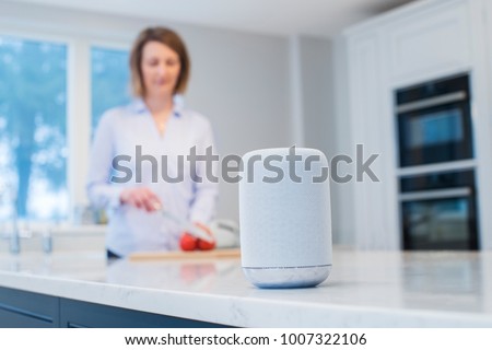 Woman Working In Kitchen With Smart Speaker In Foreground