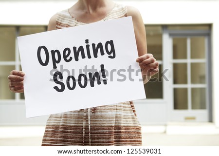 Woman Standing Outside Empty Shop Holding Opening Soon Sign