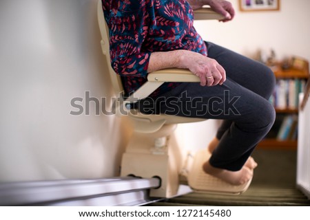 Detail Of Senior Woman Sitting On Stair Lift At Home To Help Mobility