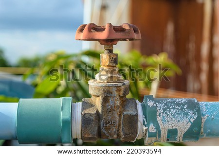 Outdoor old faucet with blue pipe on wall.