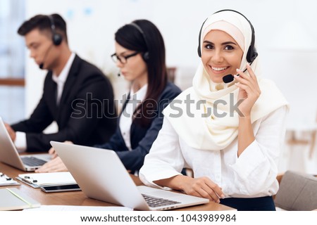 An Arab woman works in a call center. She\'s an operator. Her colleagues work nearby.