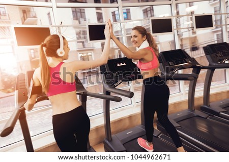 Mother and daughter in sportswear high five each other on treadmill at the gym. They look happy, fashionable and fit.