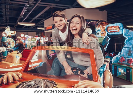 Happy mom and son sitting on toy car. Spending holiday together with family. Entertainment center, mall, amusement park. Family rest, leisure.