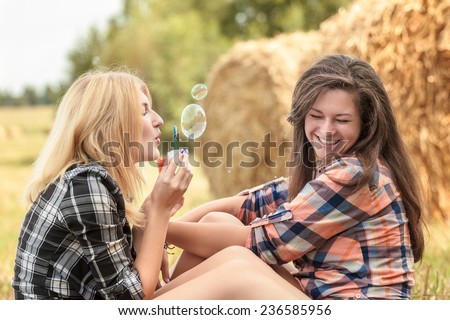 Blonde girl is blowing soap bubbles in summer day