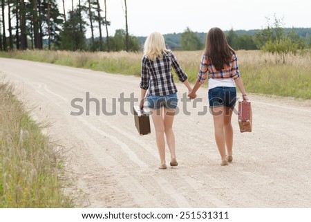 Blonde and brunette friends on country road back view