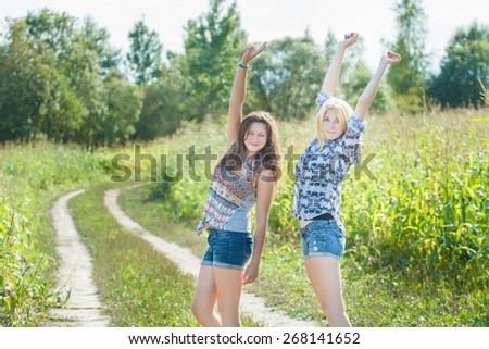 Student friends on summer rural vacations are rising arms in dance on country dirt road near corn field
