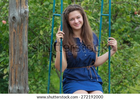 Portrait of brunette girl in navy blue sundress is sitting on handmade swing