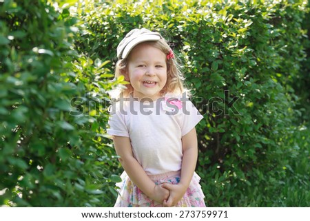 Two year-old laughing girl in corduroy flat cap and skirt at green garden shrubbery background