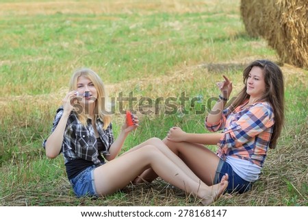 Two happy friends in summer casual cloths are making iridescent soap bubbles on summer ranch