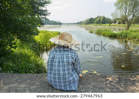 Sitting angling boy with a fishing rod on concrete bridge back view