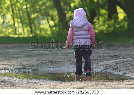 Tree years old girl is walking in summer puddle with thin tree twig in hand