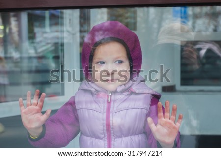Smiling toddler girl in warm hoodie pushing glass of display window