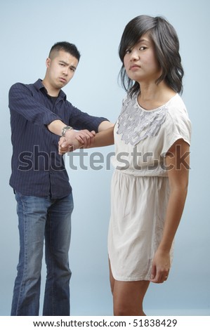 Young Asian man holding onto a young Asian woman to diffuse a situation
