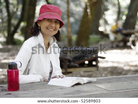 Woman sitting at a picnic table in the outdoors reading a book