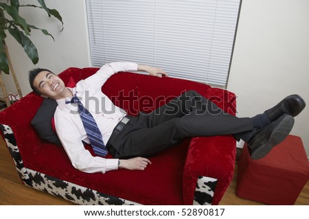 A young Asian office worker relaxes on his couch at home