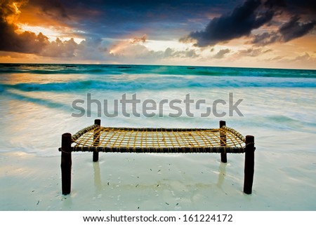 Bed on a sandy beach touching the sea under dramatic sky