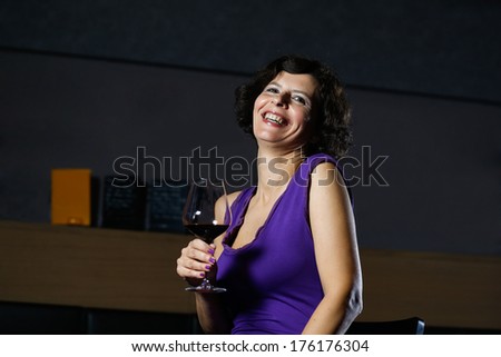 Beautiful lady in dress drinking wine and smiling in nightclub