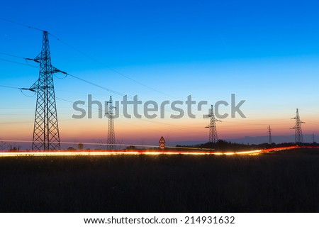 Pylons and electrical power lines at dusk with traffic lights in front