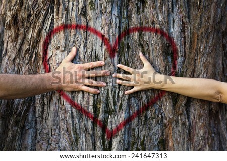 Hands of couple in love hugging a tree with painted red heart