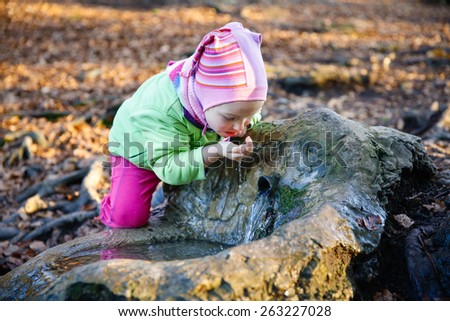 Adorable, thirsty little girl drinking clean spring water from a source in a forest