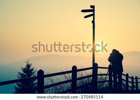 Silhouette of a photographer taking photos of an amazing sun at the top of a hill.