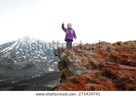 Girl celebrating reached summit on the edge of a crater on Mount Etna, volcano on the island of Sicily, Italy. Active family lifestyle, traveling family concept.