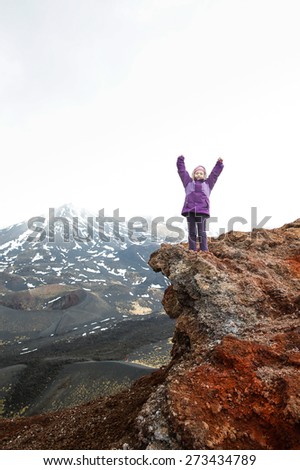 Girl celebrating reached summit on the edge of a crater on Mount Etna, volcano on the island of Sicily, Italy. Active family lifestyle, traveling family concept.