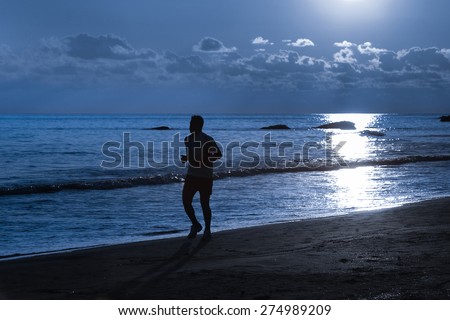 Silhouette of a fit runner in moonlight on a sandy beach in the night. Active lifestyle, vacation recreation, outdoor activity concept.