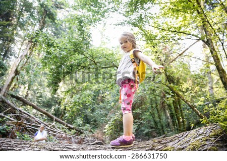 Proud little girl scout standing on a log in the woods, overcoming fear of heights, with her mother watching in the background. Active, healthy and natural lifestyle concept.