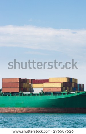 Hull of a big container ship docked in port, loaded with various colorful containers prepared for transportation. Global transportation, global business, consumerism concept and background.