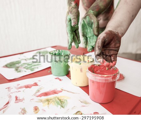 Children dipping fingers in washable, non-toxic finger paints, painting a drawing. Sensory play, permissive parenting, fun childhood concept, desaturated.