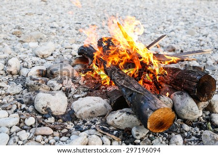 Self-made campfire on the shore of mountain river, lit for cooking, roasting and water purification. Safety and survival, fun family activity concept.