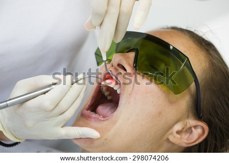 Dentist using a modern diode dental laser for periodontal care. Patient wearing protective glasses, preventing eyesight damage. Periodontitis, dental hygiene, preventive procedures concept.Ã?Â??
