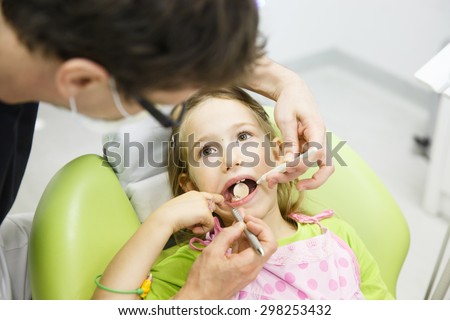 Little girl sitting on dental chair in pediatric dentists office, being examined by her dentist. Early prevention, oral hygiene and milk teeth care concept.