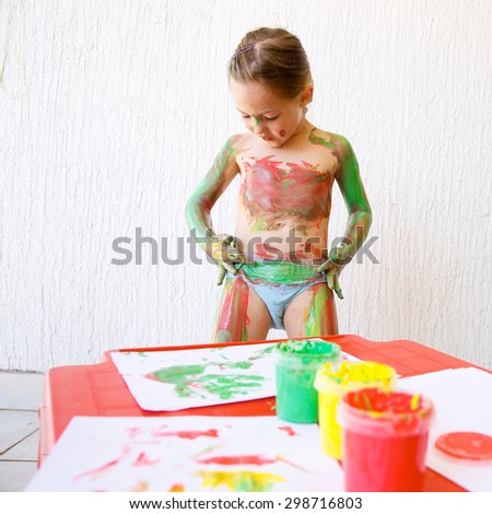 Little girl body painting herself with non-toxic, washable finger paints, having fun with creative playing. Sensory play, permissive upbringing, fun childhood concept.