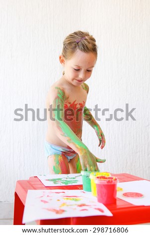 Little girl body painting herself with non-toxic, washable finger paints, having fun with creative playing. Sensory play, innovative learning, fun childhood concept.