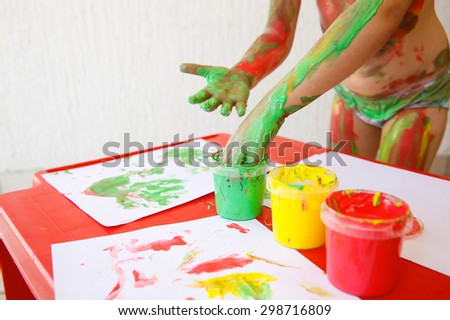 Child dipping fingers in washable, non-toxic finger paints, painting a drawing. Sensory play, innovative approach to learning, fun childhood concept.