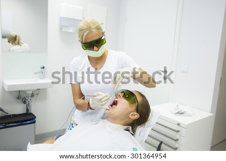 Dental hygienist using a modern diode dental laser for periodontal care, wearing protective glasses, preventing eyesight damage. Periodontitis, dental hygiene, preventive procedures concept.