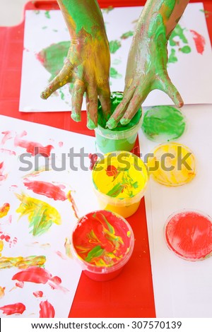Child dipping fingers in washable, non-toxic finger paints, painting a drawing. Sensory play, innovative approach to learning, fun childhood, back to school concept.