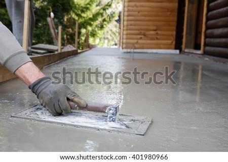 Mason leveling and screeding concrete floor base with square trowel in front of the house. Construction business, do-it-yourself, precision work around the house concept.