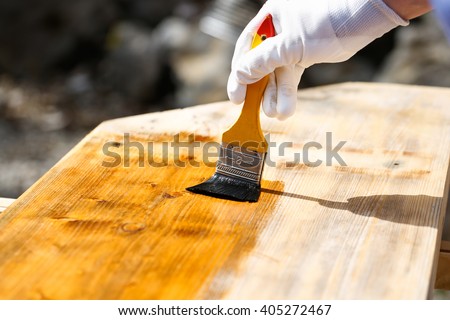 Painter holding a paintbrush over wooden surface, protecting wood for exterior influences and weathering. Carpentry, wood treatment, hard at work, home improvement, do-it-yourself concept.