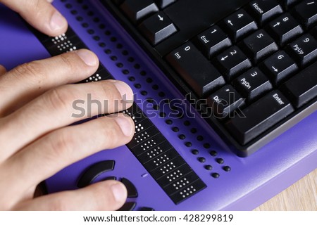 Blind person using computer with braille computer display and a computer keyboard. Blindness aid, visual impairment, independent life concept.