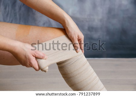 Woman patient with varicose veins applying elastic compression bandage after surgery. Curative treatment, thrombosis prevention and senior health care concept.