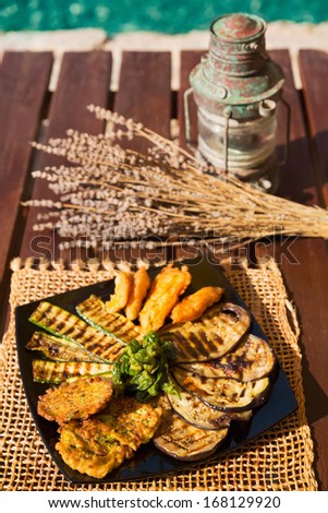 Serving of grilled zucchini, chicken and eggplant blue/Plate of plenty grilled food on picnic table. Lantern on serving table with serving plate. Grilled vegetable.