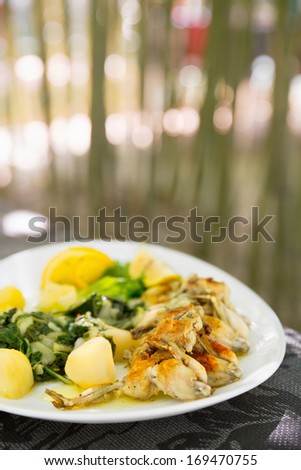 Lunch, frogs legs/Serving plate with crisp frog legs with potatoes and chard, Lemon decoration with green vegetable.