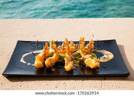 Serving plate with crispy shrimps and salad/Colorful dishware with seafood and vegetables. Delicious seafood serving on picnic table.