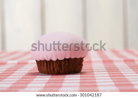 Chocolate cupcake covered with pink fondant. Cupcake on picnic table./Chocolate cupcake