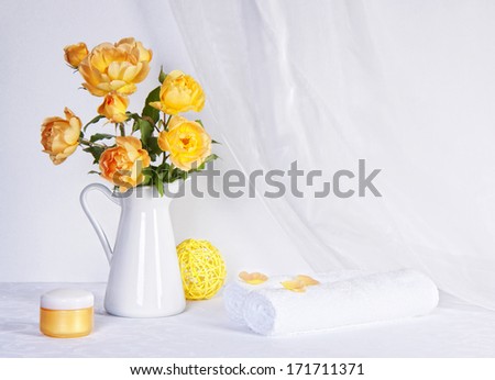 Still life with a picture set for spa with cream jars, yellow roses in a white vase and towels on white background